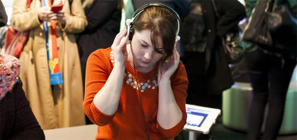Woman with red hair dressed in orange wearing headphones is playing a video game