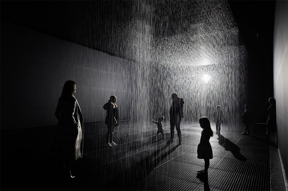 People walking in a dark room with rain falling from the ceiling