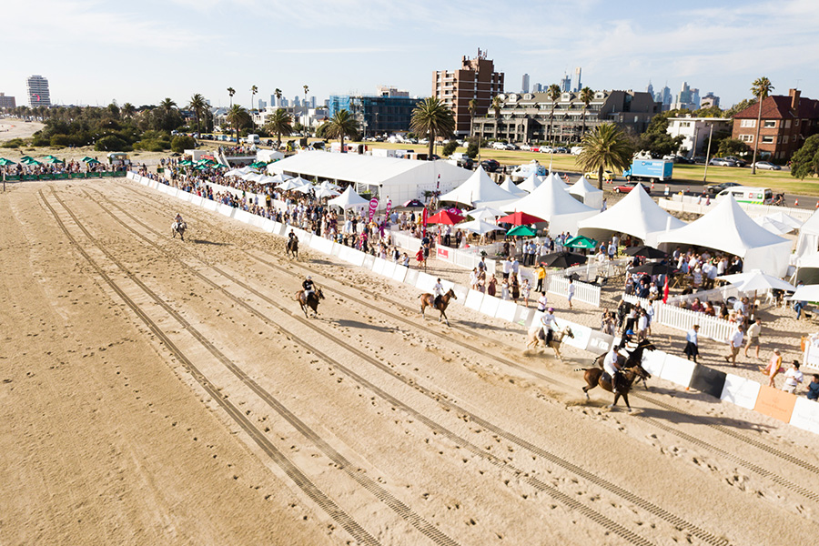 A polo match being played on a beach in front of a big crowd